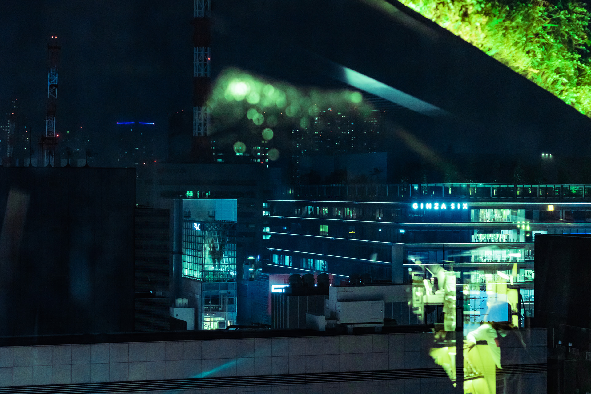Night time skyline view from a rooftop with bright green reflections in glass in the foreground.